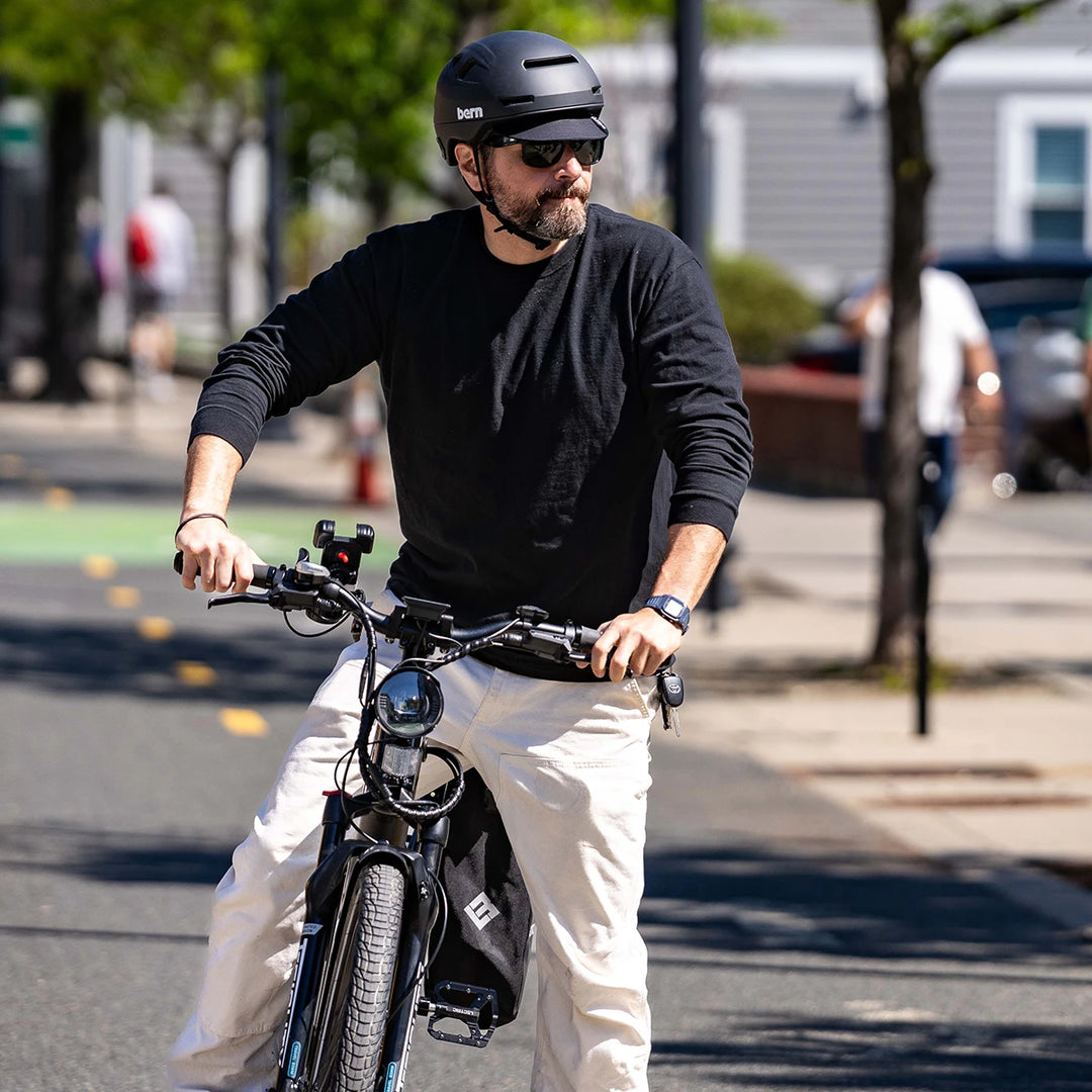 Man riding an e-bike on a city street, wearing a Bern Hudson MIPS helmet, matte black.