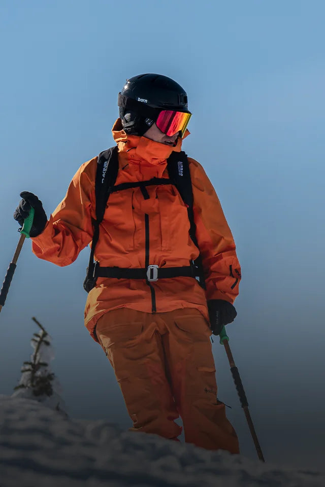 Rider wearing Bern Hendrix En1077B certified winter helmet atop snowy mountain.