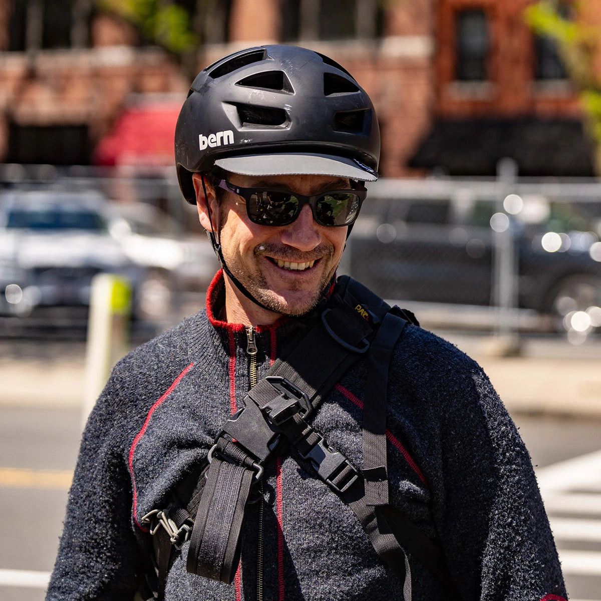 Man wearing a black bern Allston bike helmet and sunglasses on a city street.