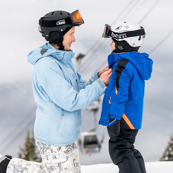 Mother and son wearing Bern snow helmets and goggles at ski resort.