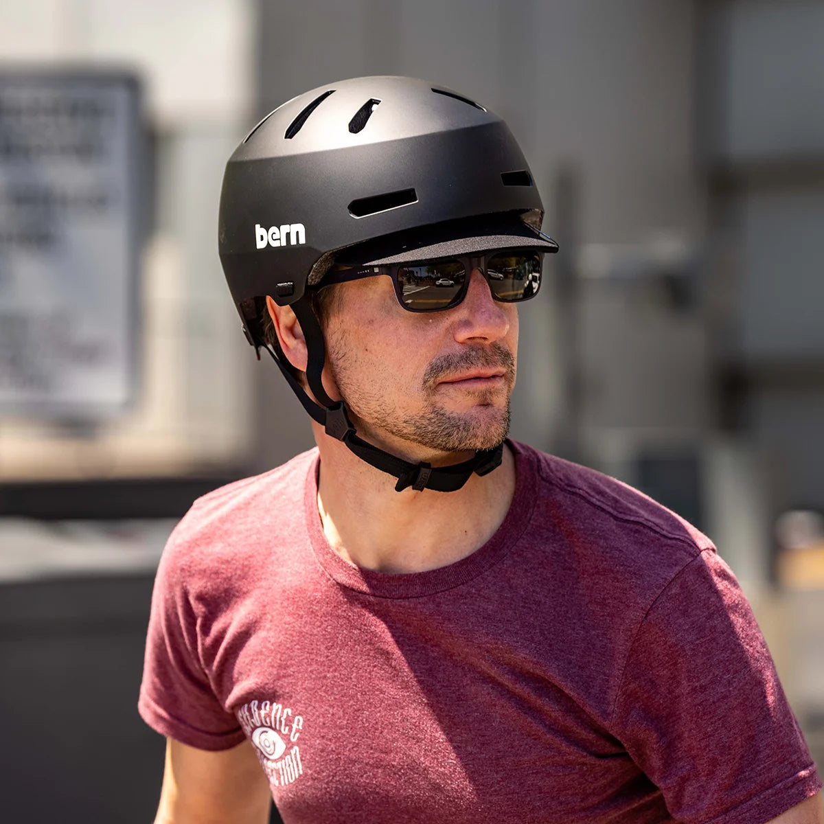 Man wearing Macon 2.0 bike helmet, matte black, with add on flip visor attachment, while riding a bicycle